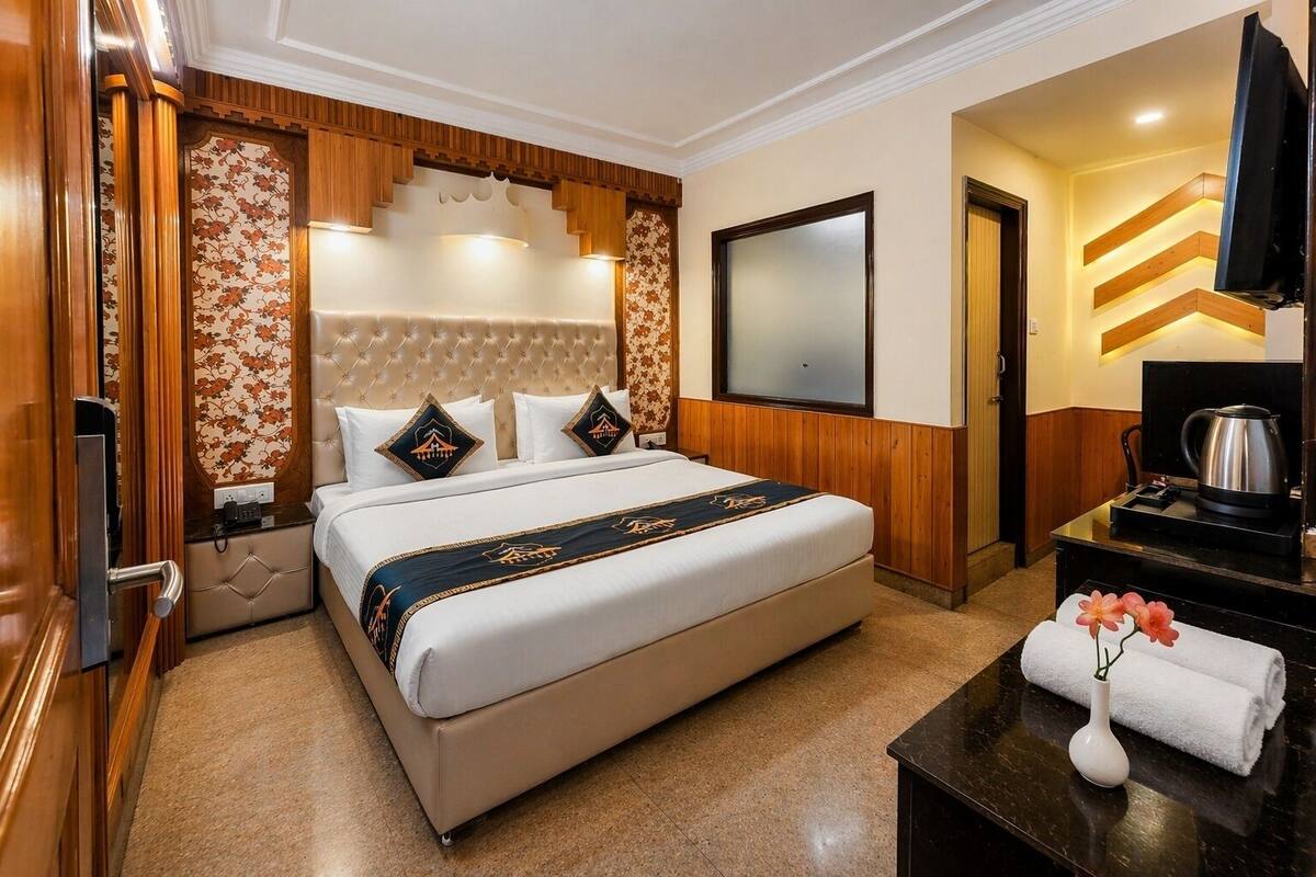 A hotel room with a bed, a flat-screen TV, a coffee maker, and a desk with a vase of flowers.
