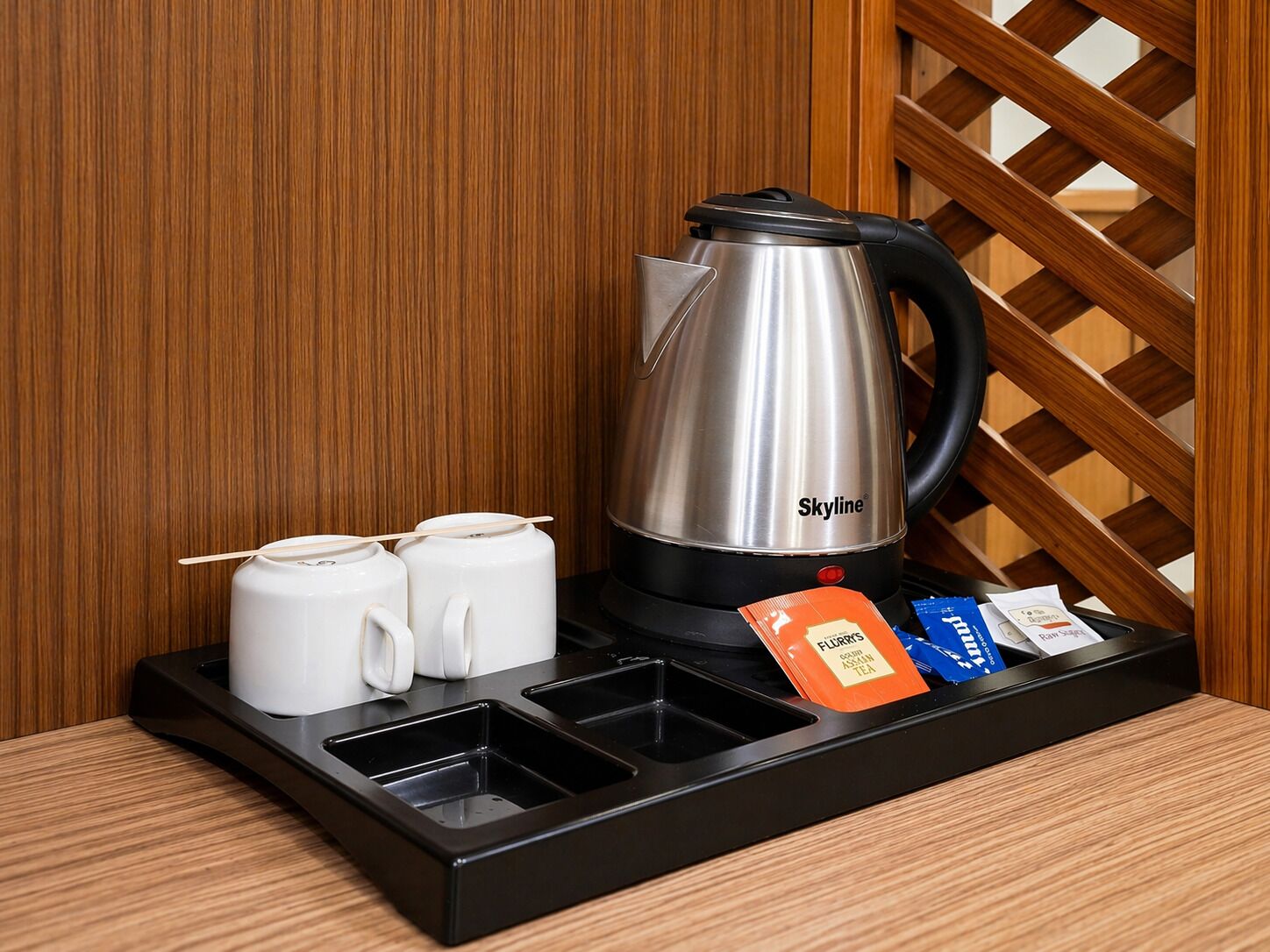 A stainless steel kettle, two white mugs, and tea packets on a tray.