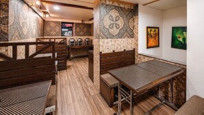 A restaurant interior with wooden benches, a high ceiling with a geometric pattern, and a tiled wall with a mosaic design.