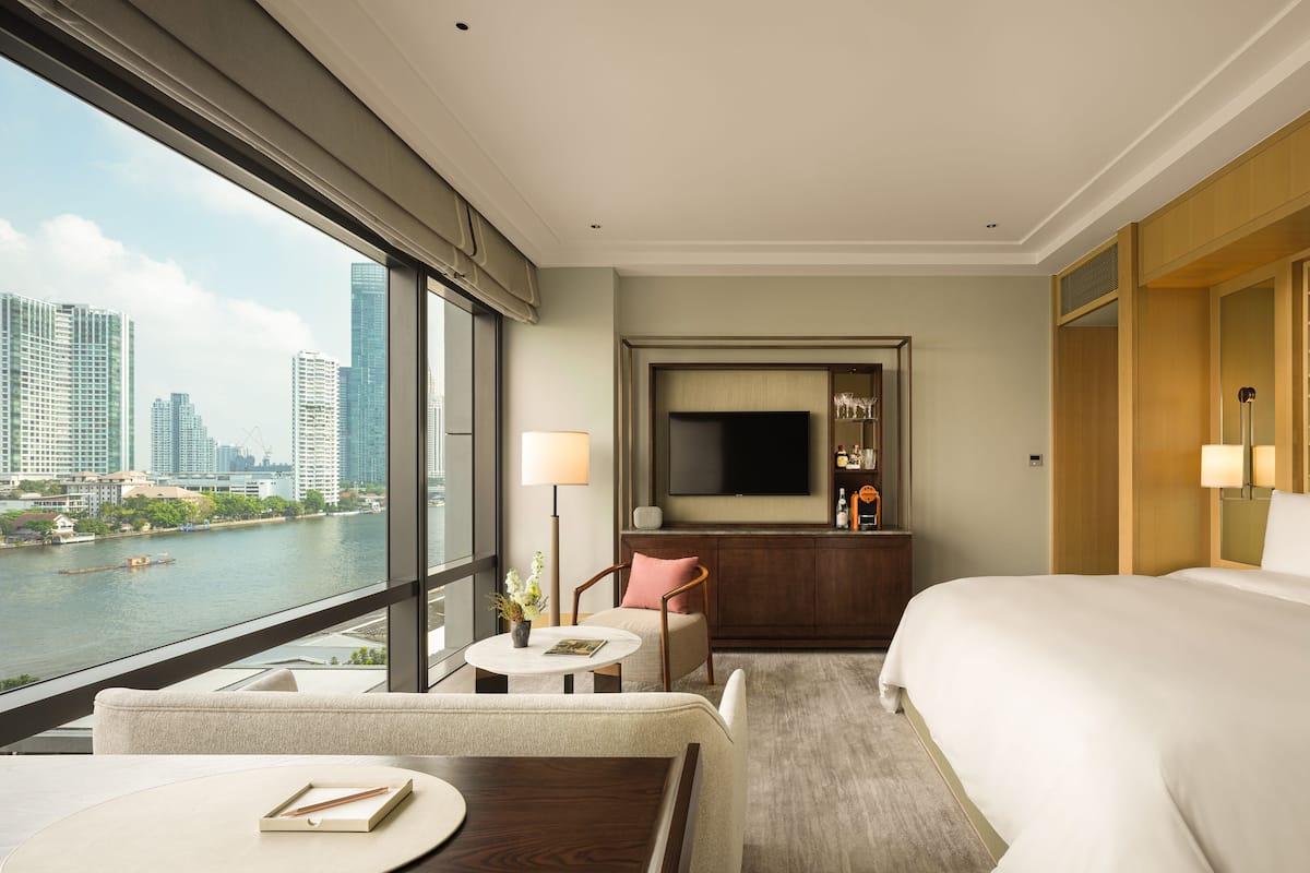 A hotel room with a large bed, a desk with a chair, a small table, a sofa, and a TV mounted on the wall.