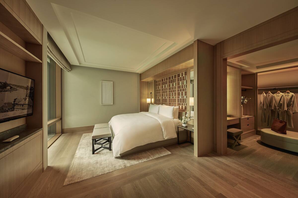 A modern hotel room with a large bed, bedside tables, a wardrobe, and a desk.