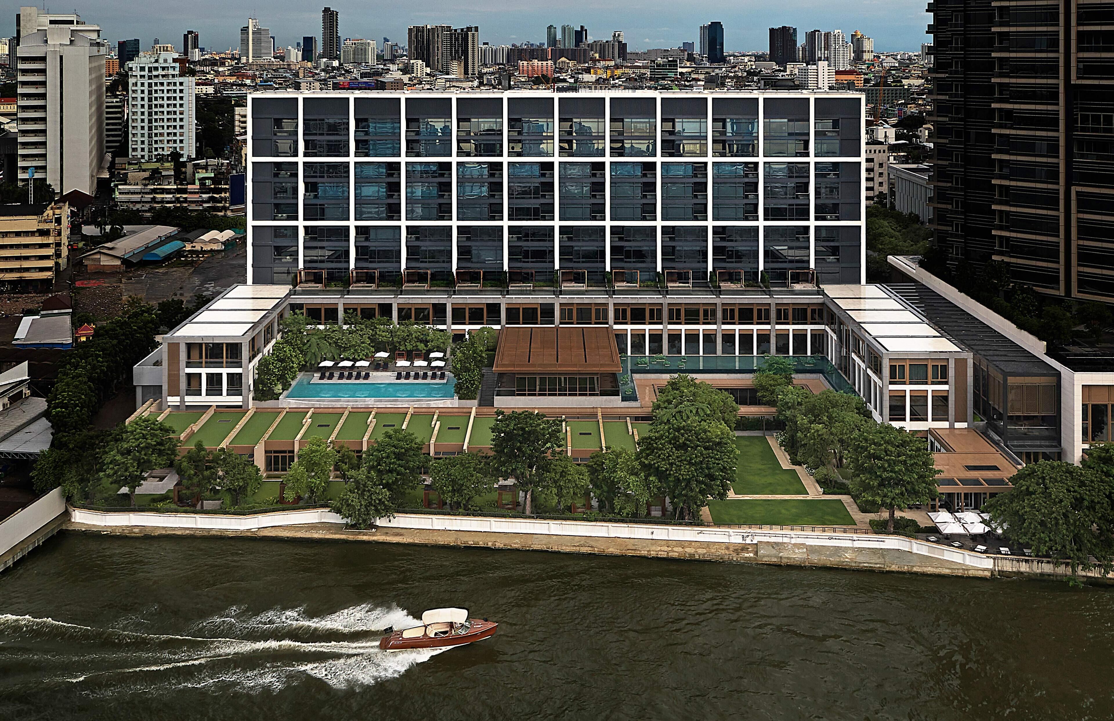 Un edificio moderno con piscina, rodeado de vegetación y un río.