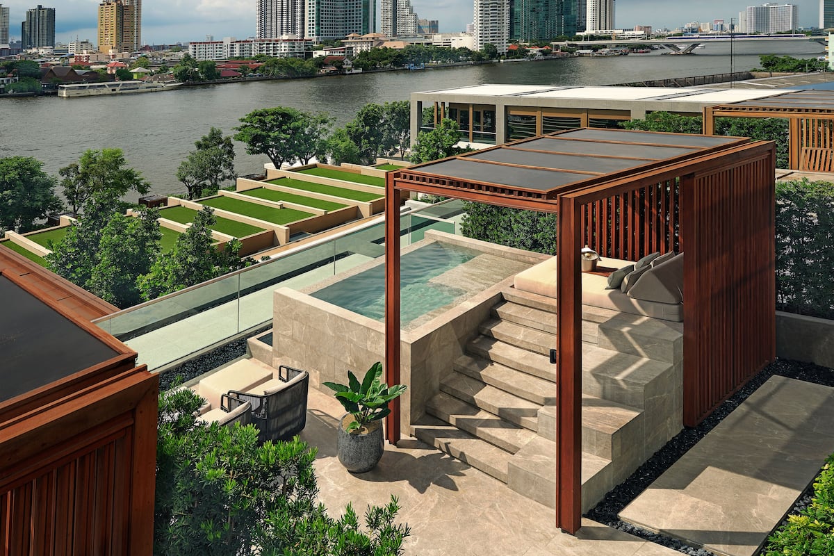 A rooftop terrace with a pool, outdoor seating, and a view of the city skyline across a river.