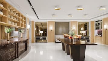 A modern hotel lobby with marble flooring, a central dining table, and a variety of amenities including a reception desk, seating areas, and decorative lighting.