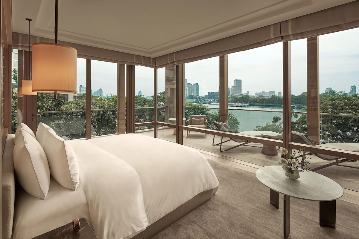A modern hotel room with a large bed, a small table with a vase, and a balcony with a view of the city and river.