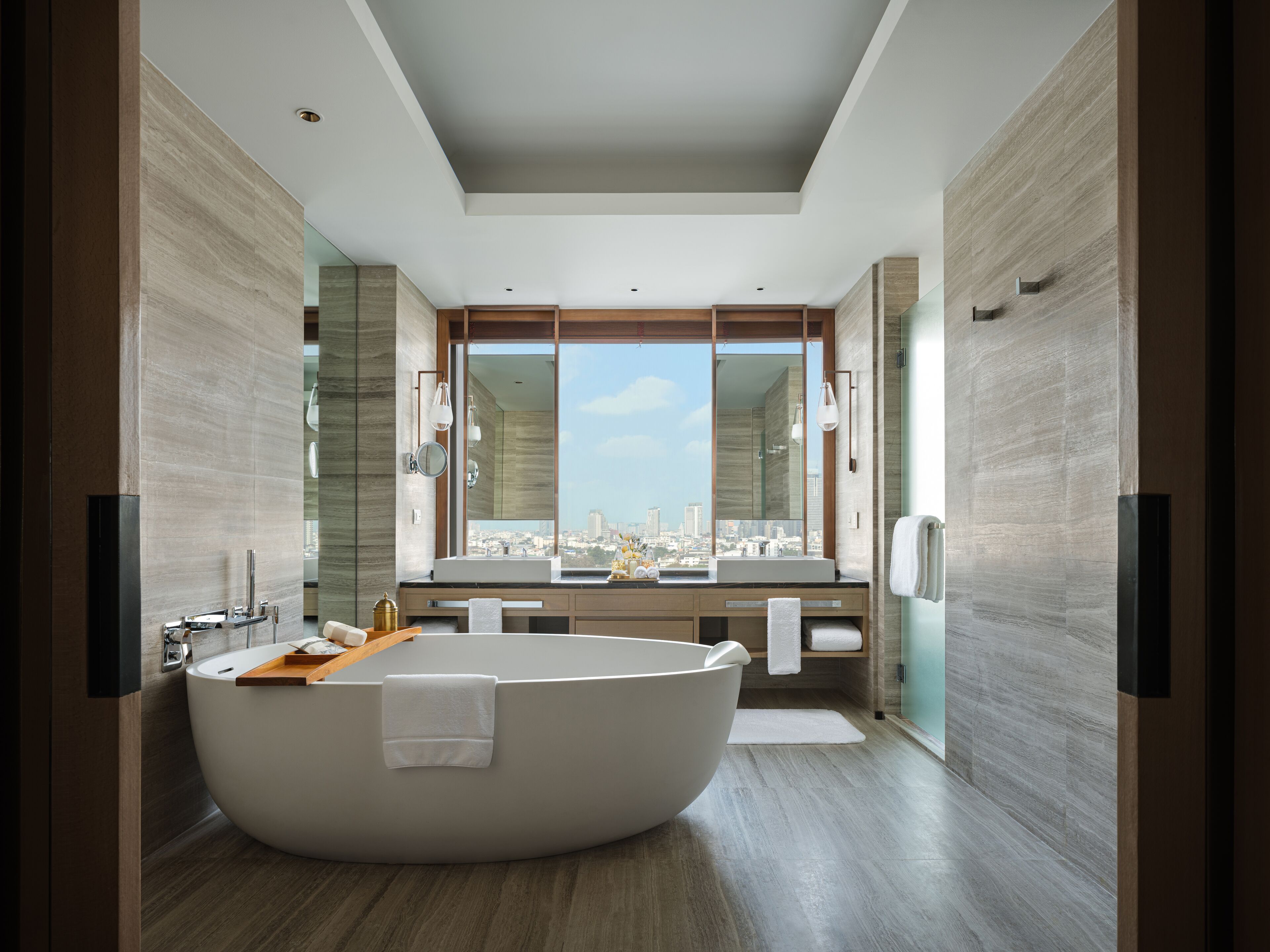 A modern bathroom with a freestanding bathtub, a large mirror, and a view of a cityscape.
