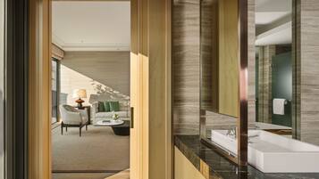 A modern hotel room with a large mirror, a bathtub, and a seating area with a sofa and coffee table.