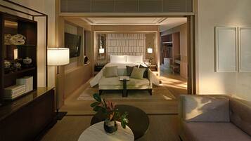 A modern hotel room with a large bed, bedside lamps, a sofa, a small table with a vase, and a bookshelf.