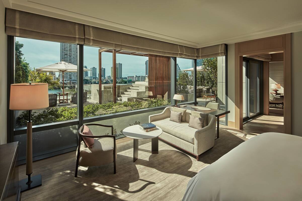 A modern hotel room with a large window, a sofa, a coffee table, and a lamp.