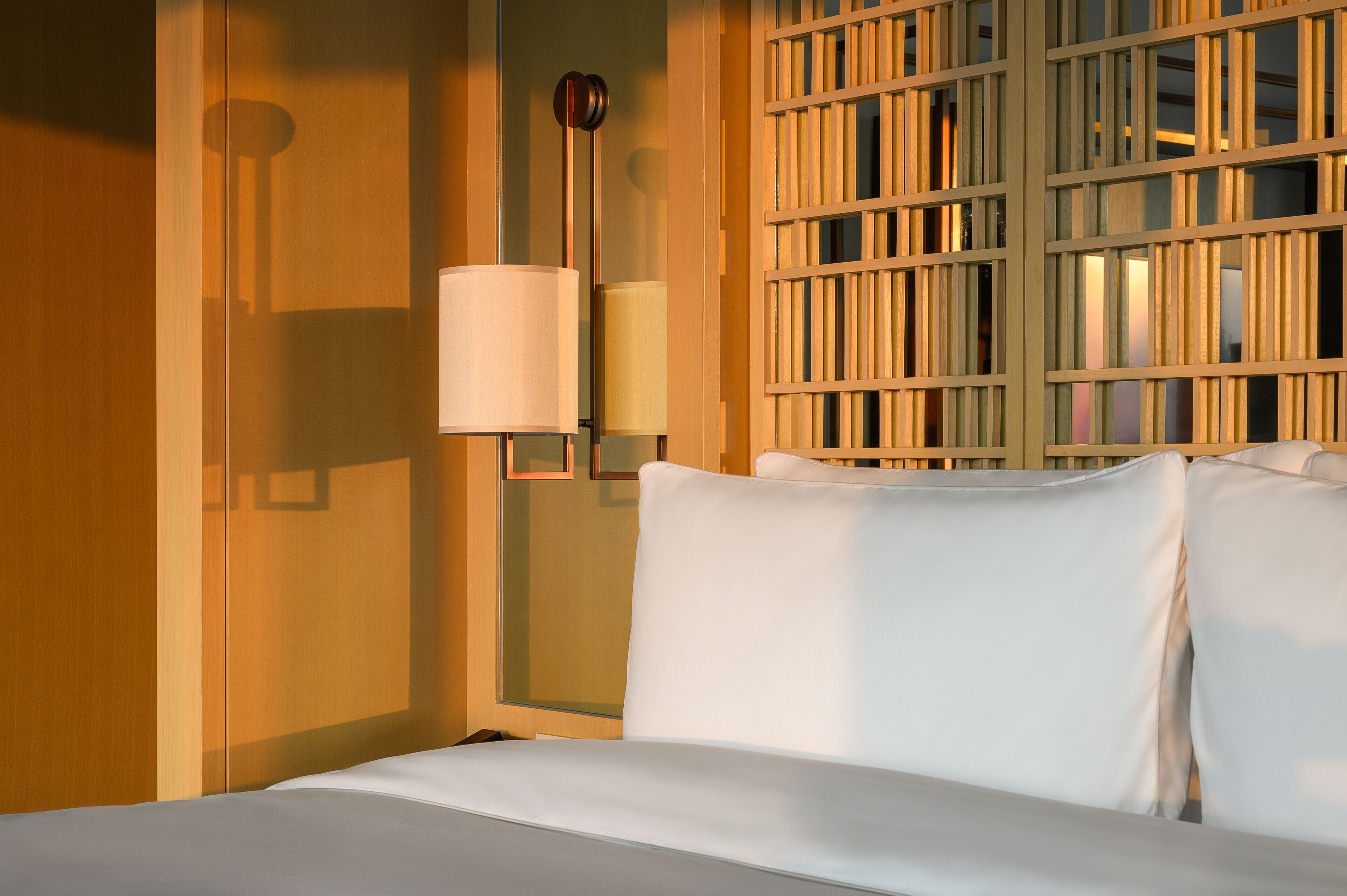 Una habitación de hotel con una cama, una lámpara fijada a la pared y un panel de madera con listones verticales.