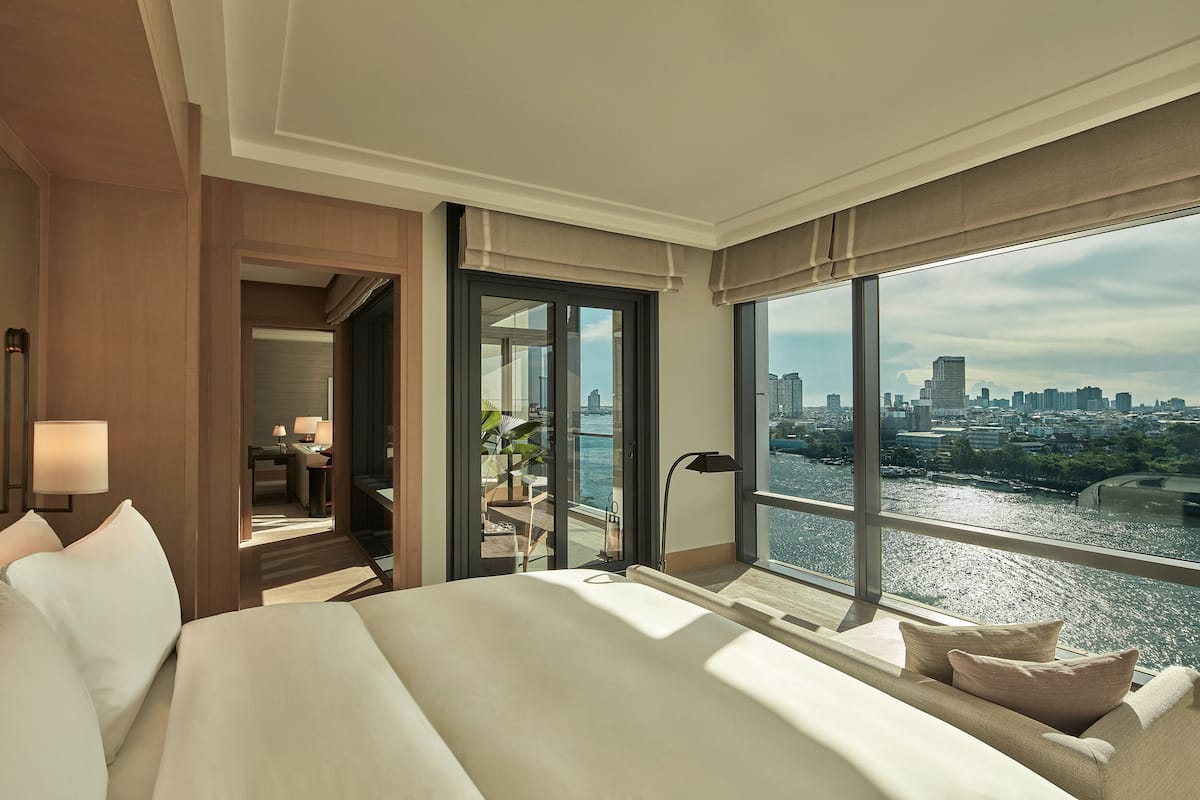 A hotel room with a large bed, a desk, and a view of a cityscape and river.