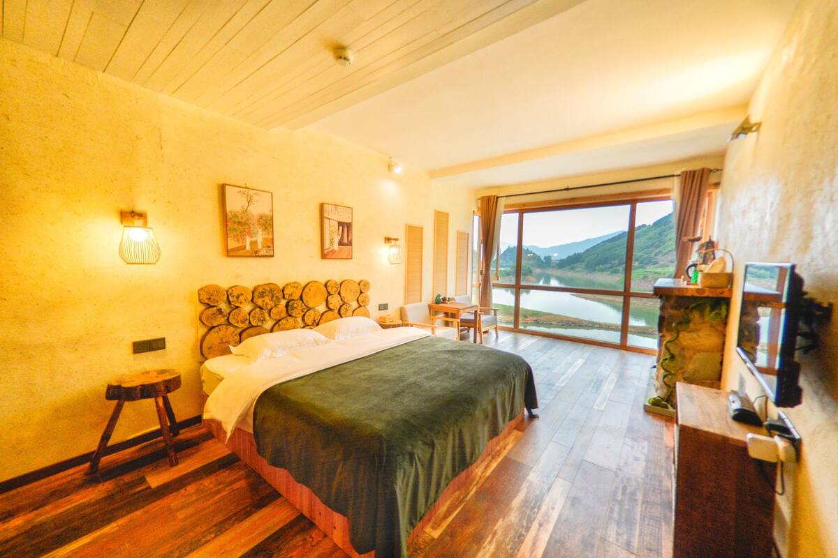 Une chambre dotée d’un grand lit, d’un parquet en bois, d’une cheminée en pierre et offrant une vue sur l’extérieur.