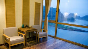 A room with a large window offering a view of a river and mountains. There is a wooden table with two chairs. - Floral Hotel Qiandaohu Deyishe Inn (Hangzhou)