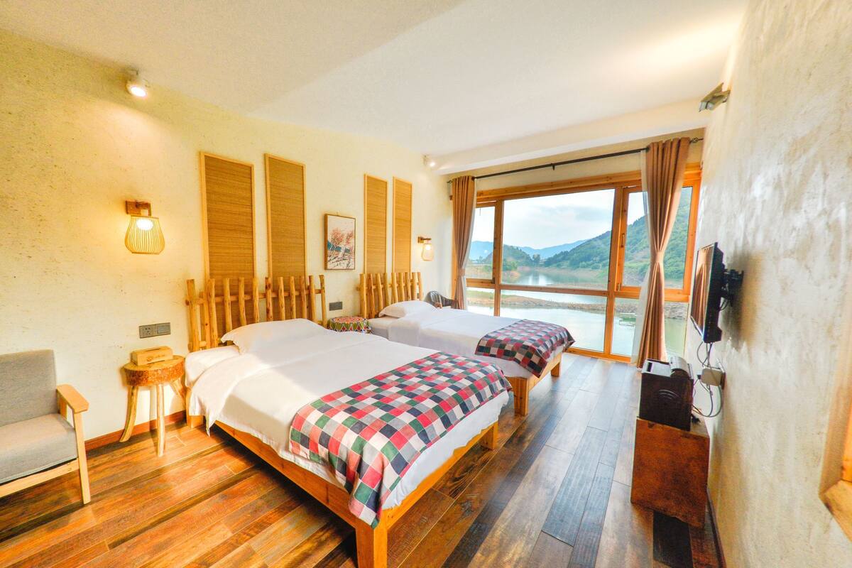 Une chambre d’hôtel avec deux lits, une chaise, une petite table et une grande fenêtre donnant sur un paysage magnifique.
