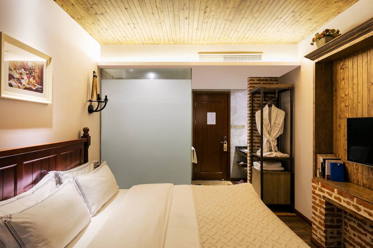 Hotellihuone, jossa on puinen katto, valkoisilla lakanoiden peitetty sänky, puinen vaatekaappi ja televisio puisen lipaston päällä.