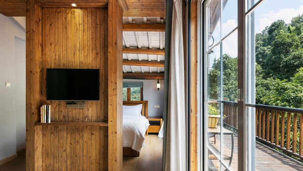A bedroom with a wooden ceiling, a TV mounted on the wall, a bed, and a window overlooking a deck. - Floral Hotel Hangzhou Nuanshuyiju (Hangzhou)