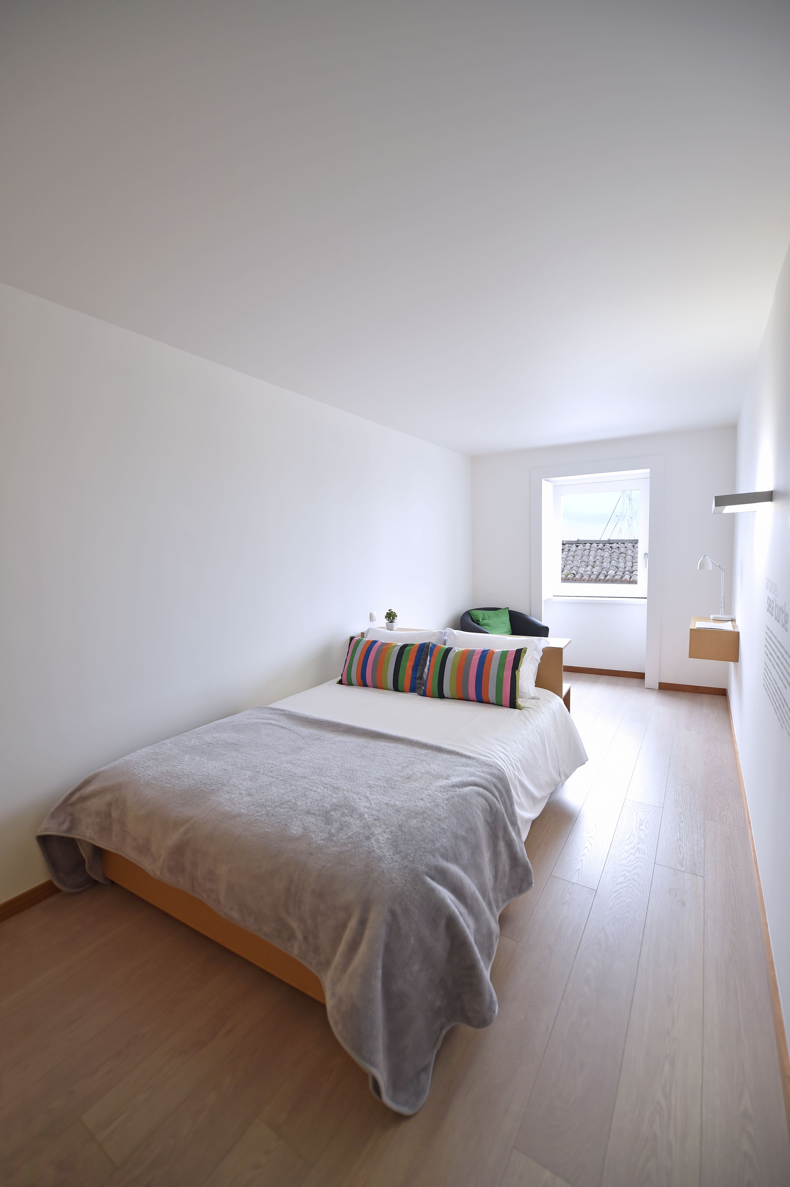 A minimalist bedroom with a bed, a chair, a window, and a bedside table.