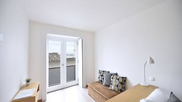 A minimalist bedroom with a bed, a nightstand, a desk with a lamp, and a sliding door leading to a balcony.