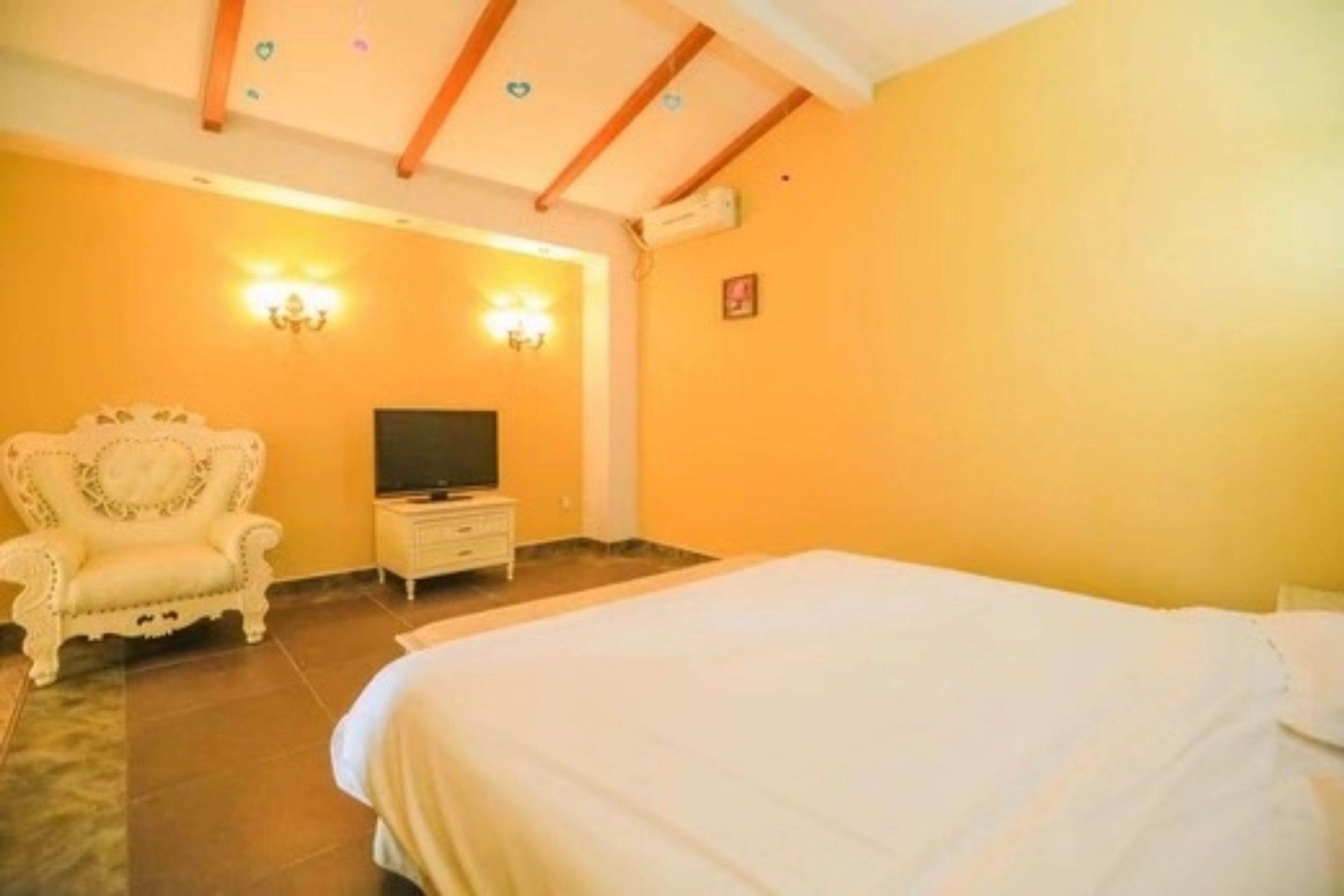 A bedroom with a bed, a TV, a chair, and wall sconces.
