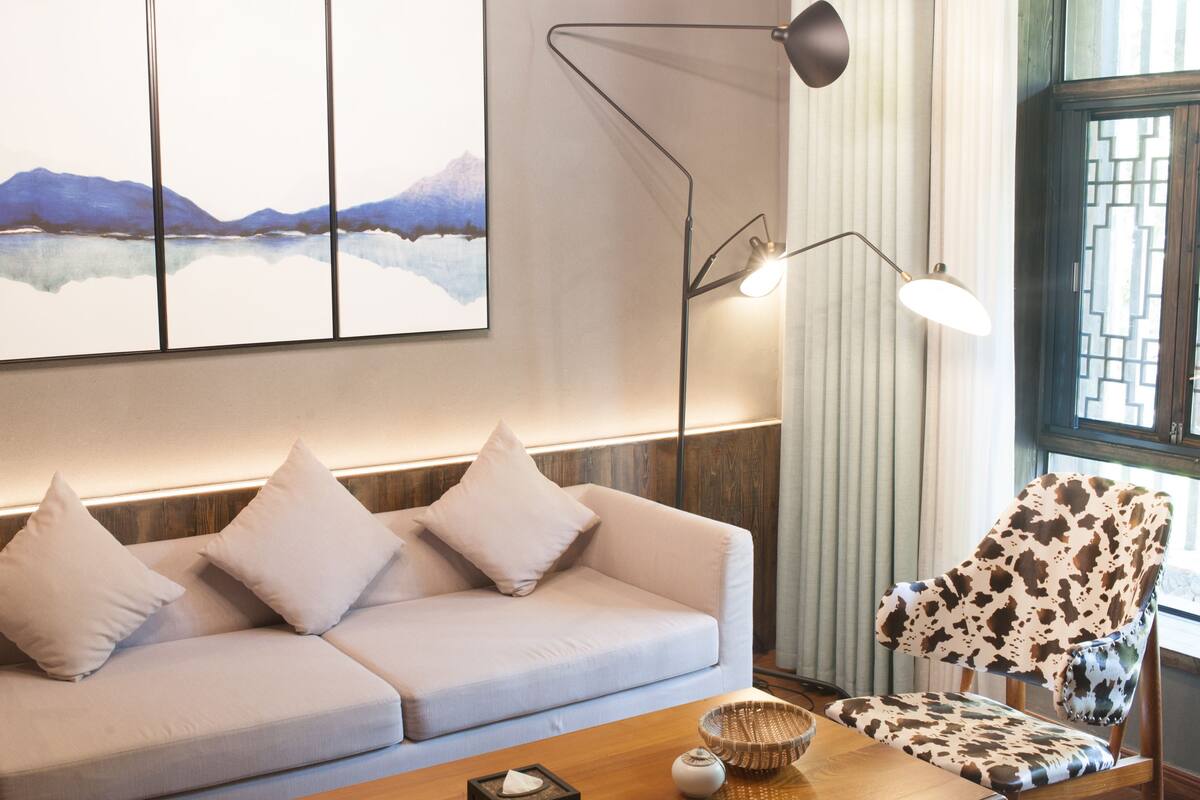 Un soggiorno moderno con un divano chiaro, una poltrona fantasia e un grande quadro astratto appeso al muro.
