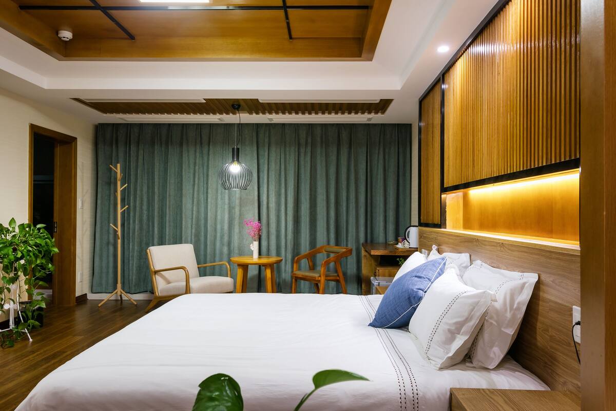 A hotel room with a large bed, a desk, a chair, and a potted plant.
