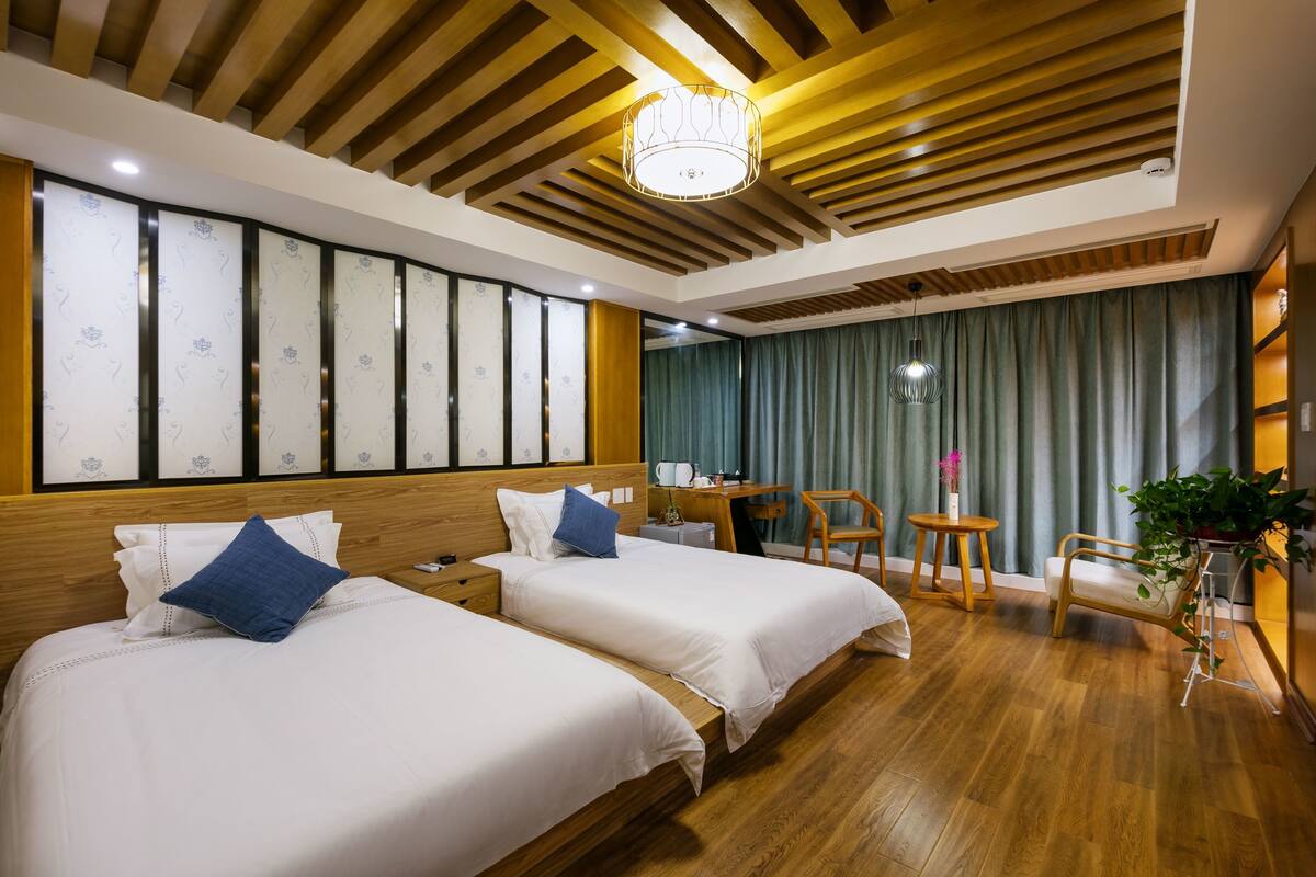 A hotel room with two beds, wooden ceiling, and a desk with a chair.