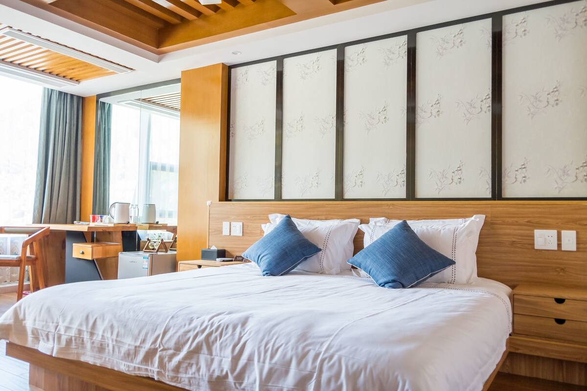 A hotel room with a large bed, wooden headboard, and a desk with a chair.