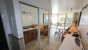 Une cuisine moderne avec une porte-fenêtre coulissante donnant sur un balcon, un coin repas avec un canapé et une table, et une salle de bain avec douche et toilettes.