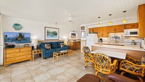 Un salon moderne avec un canapé bleu, des meubles en bois et un coin cuisine doté de meubles de rangement en bois et d’un plan de travail blanc.