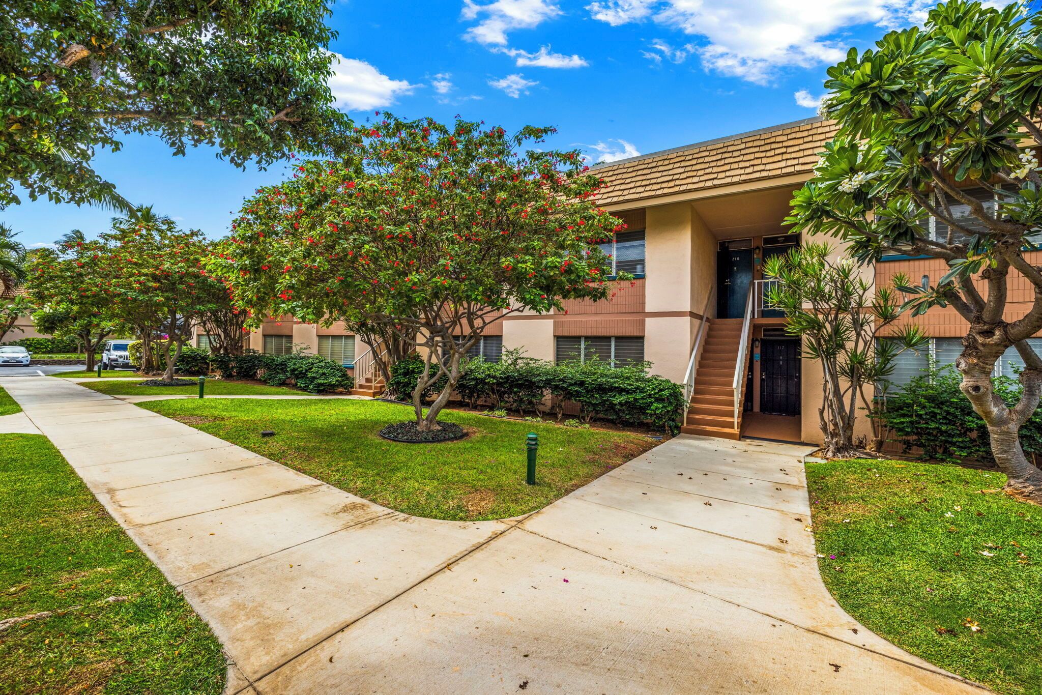 A residential building with a modern design, featuring a central entrance with a staircase, surrounded by well-maintained lawns and trees.