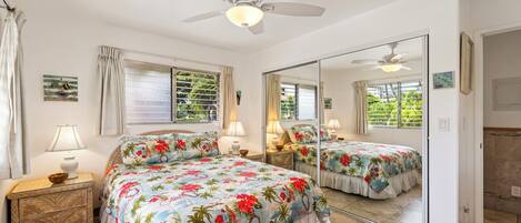 A bedroom with a bed, a ceiling fan, a nightstand, a mirror, and a window with curtains.