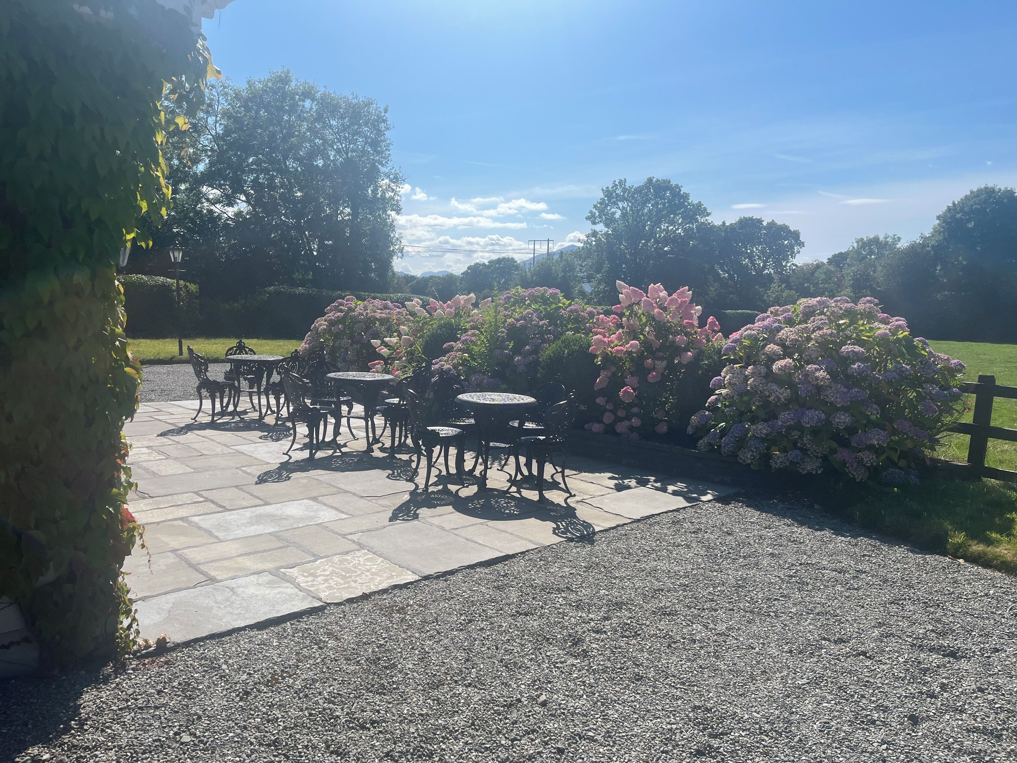 Een terras buiten met stenen vloer en metalen tafels en stoelen.