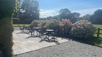 Een terras buiten met stenen vloer en metalen tafels en stoelen.