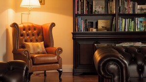 A leather armchair with a cushion, a bookshelf filled with books, and a lamp.