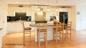 A modern kitchen with white cabinetry, a central island with stools, a stove, and a refrigerator.