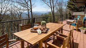 Una terraza de madera con una mesa y sillas, un jarro de té helado y una bandeja con aperitivos.