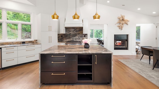 Una cocina moderna con una isla grande, armarios oscuros y una chimenea.