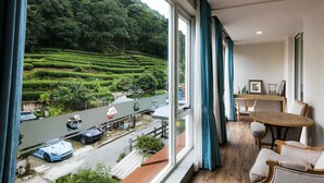 A room with a large window offering a view of a lush green hillside and a road with parked cars. - Floral Hotel Hangzhou Yunqi Fanjinglan (Hangzhou)