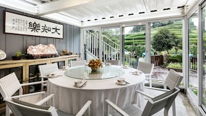 A round dining table with white chairs, a glass top, and a vase of flowers. There is a staircase leading to a garden with a view of green hills. - Floral Hotel Hangzhou Yunqi Fanjinglan (Hangzhou)