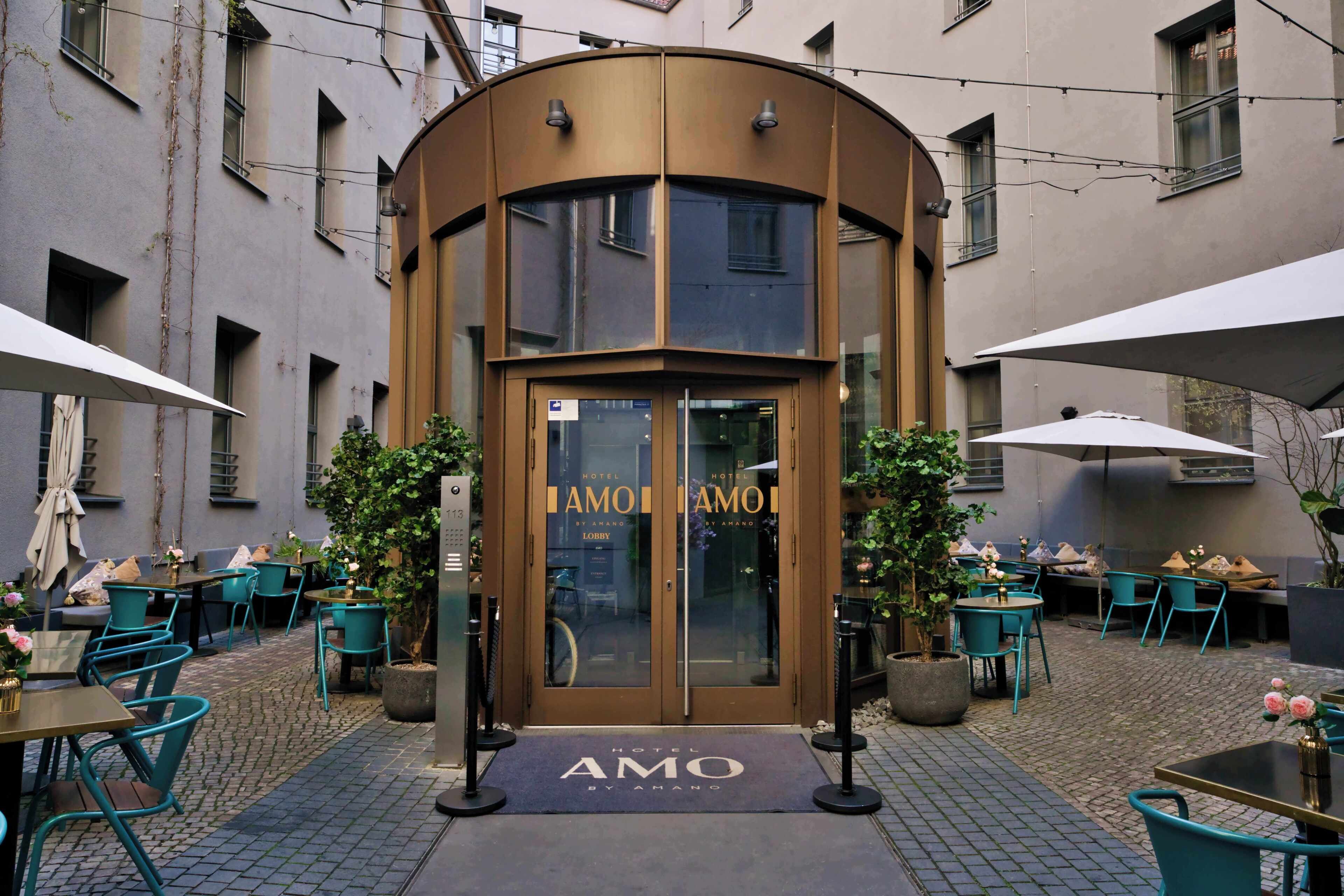 A hotel entrance with a curved facade, outdoor seating, and potted plants.
