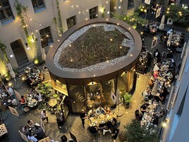 An outdoor dining area with tables and chairs, surrounded by a circular structure with a garden in the center.