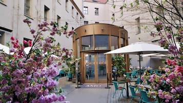 Um café com mesas ao ar livre, entrada curva e um letreiro 'AMO' visível.
