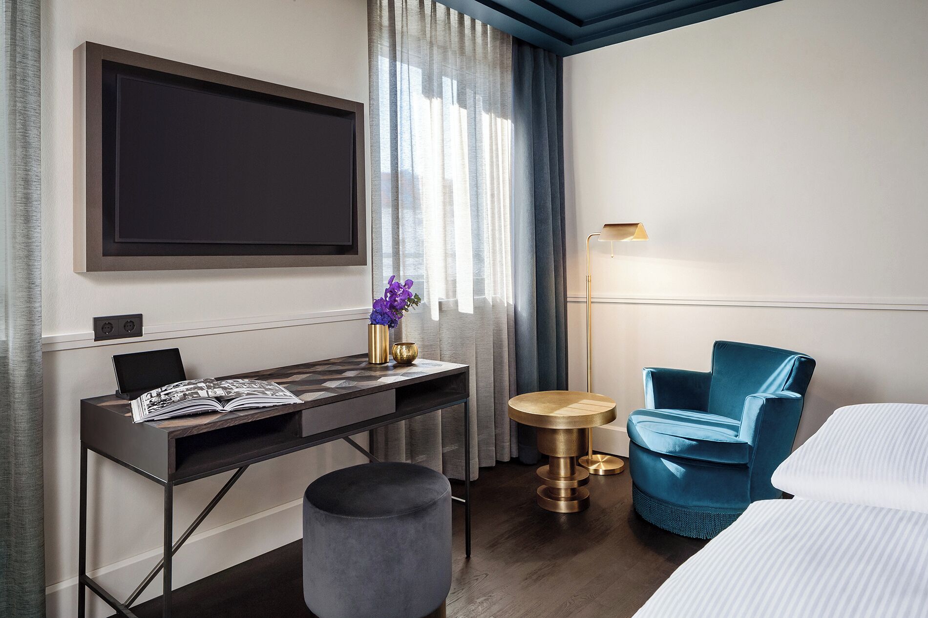 Ein Hotelzimmer mit einem Bett, einem Schreibtisch mit einem Laptop, einem Sessel, einem runden Tisch und einem an der Wand befestigten Fernseher.