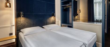 Habitación de hotel con cama doble, cabecera azul oscuro, espejo y armario.