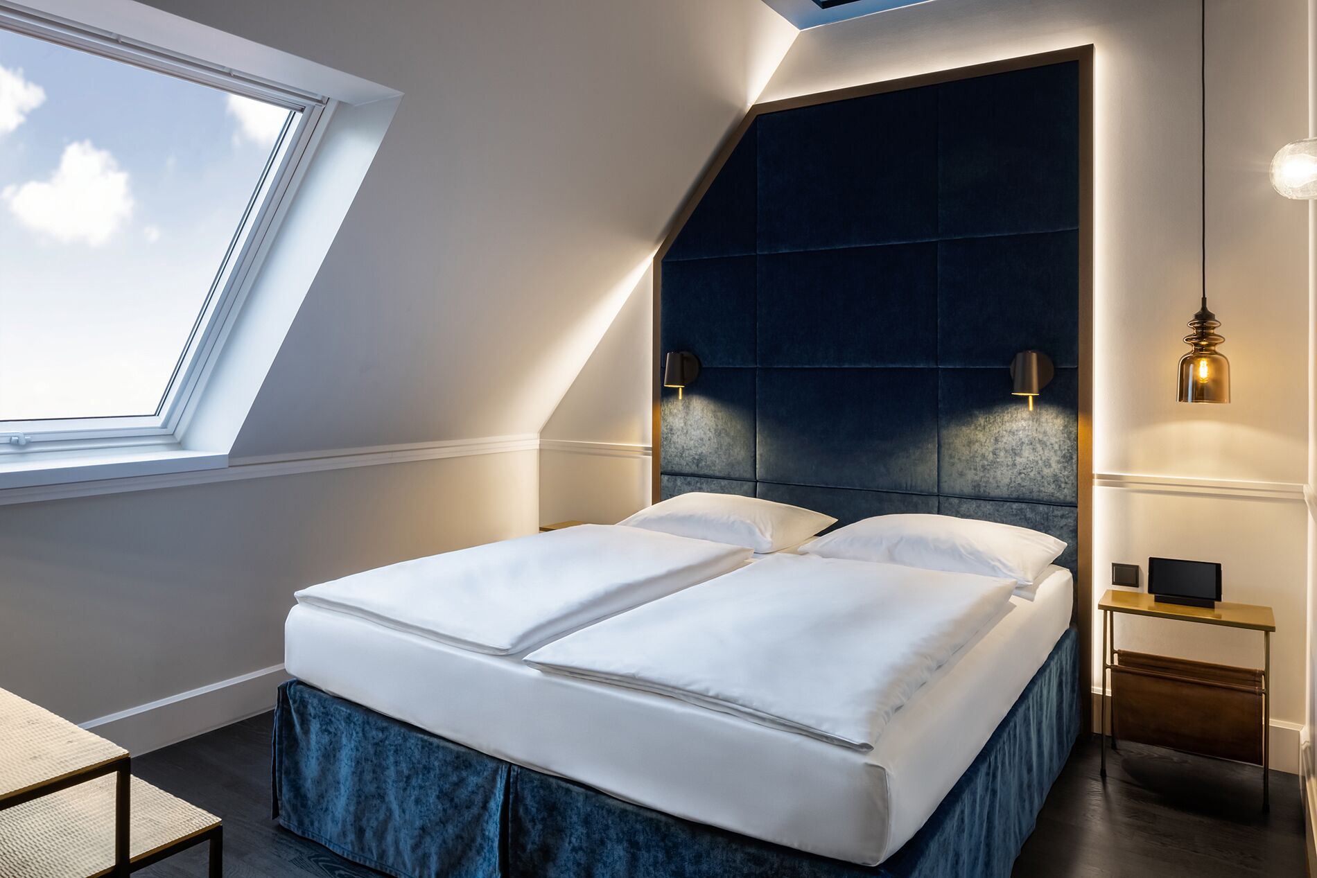 A modern bedroom with a skylight, a dark headboard, and a bedside table with a lamp.