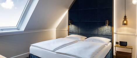 A modern bedroom with a skylight, a dark headboard, and a bedside table with a lamp.