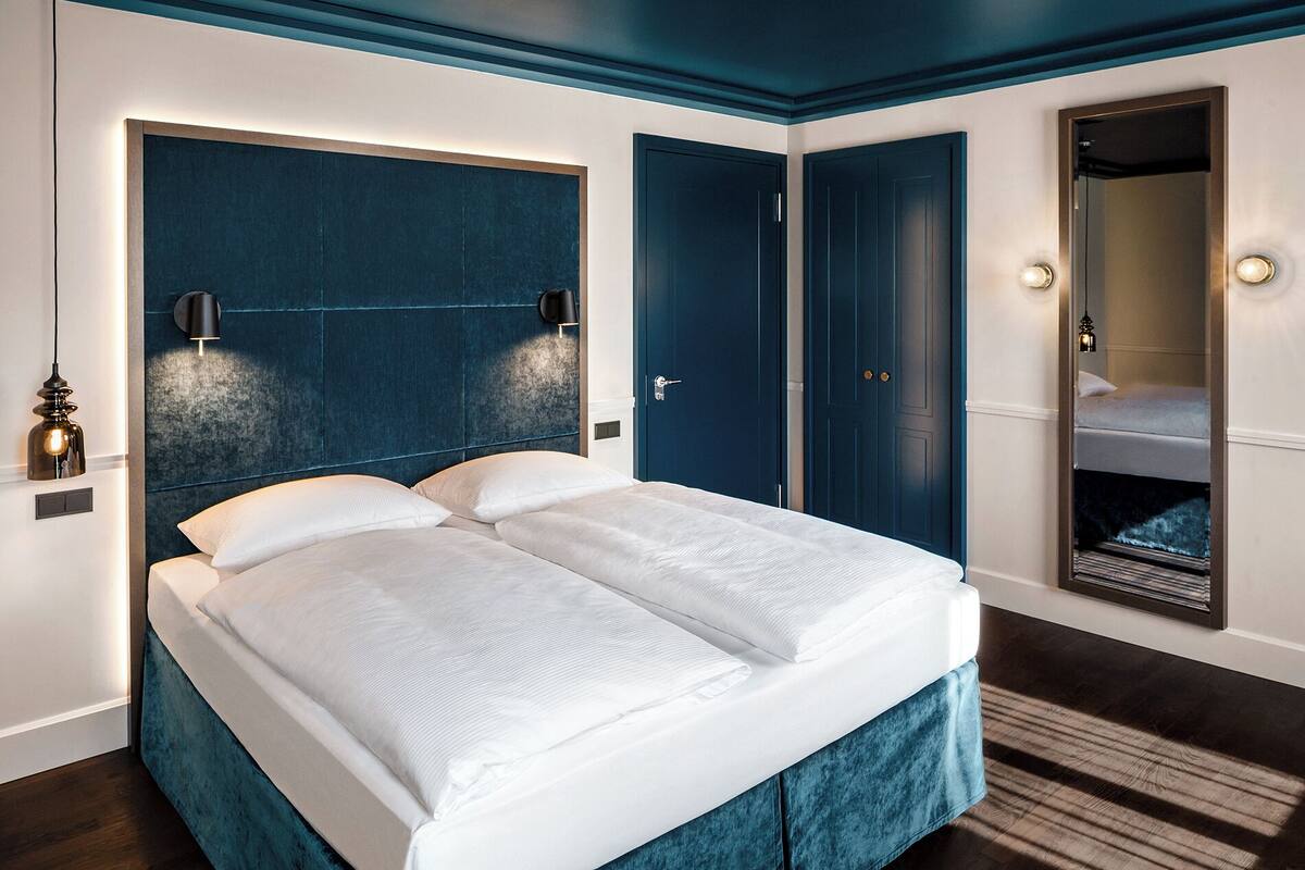 Un dormitorio moderno con una cama grande, cabecera azul oscuro y un espejo.