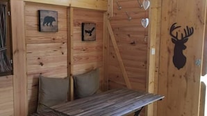 A cozy wooden cabin interior with a loft bed, a small table, and a bench.