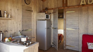 A rustic wooden cabin with a kitchen area featuring a stove, sink, refrigerator, and a microwave.