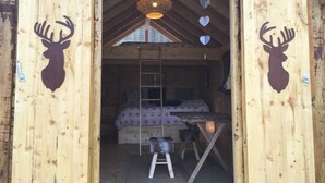 A wooden cabin with a loft bed, a ladder, and a hanging light fixture.